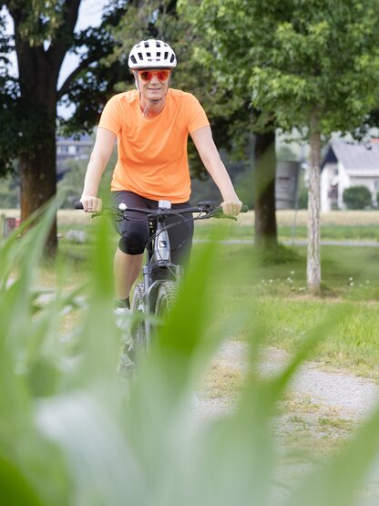 Maria Höfl-Riesch mit Helm auf dem Mountainbike inmitten grüner Landschaft unterwegs