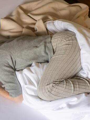 Frau in Loungewear zusammengerollt im Bett – Rückzug und Ruhe bei Regelschmerzen