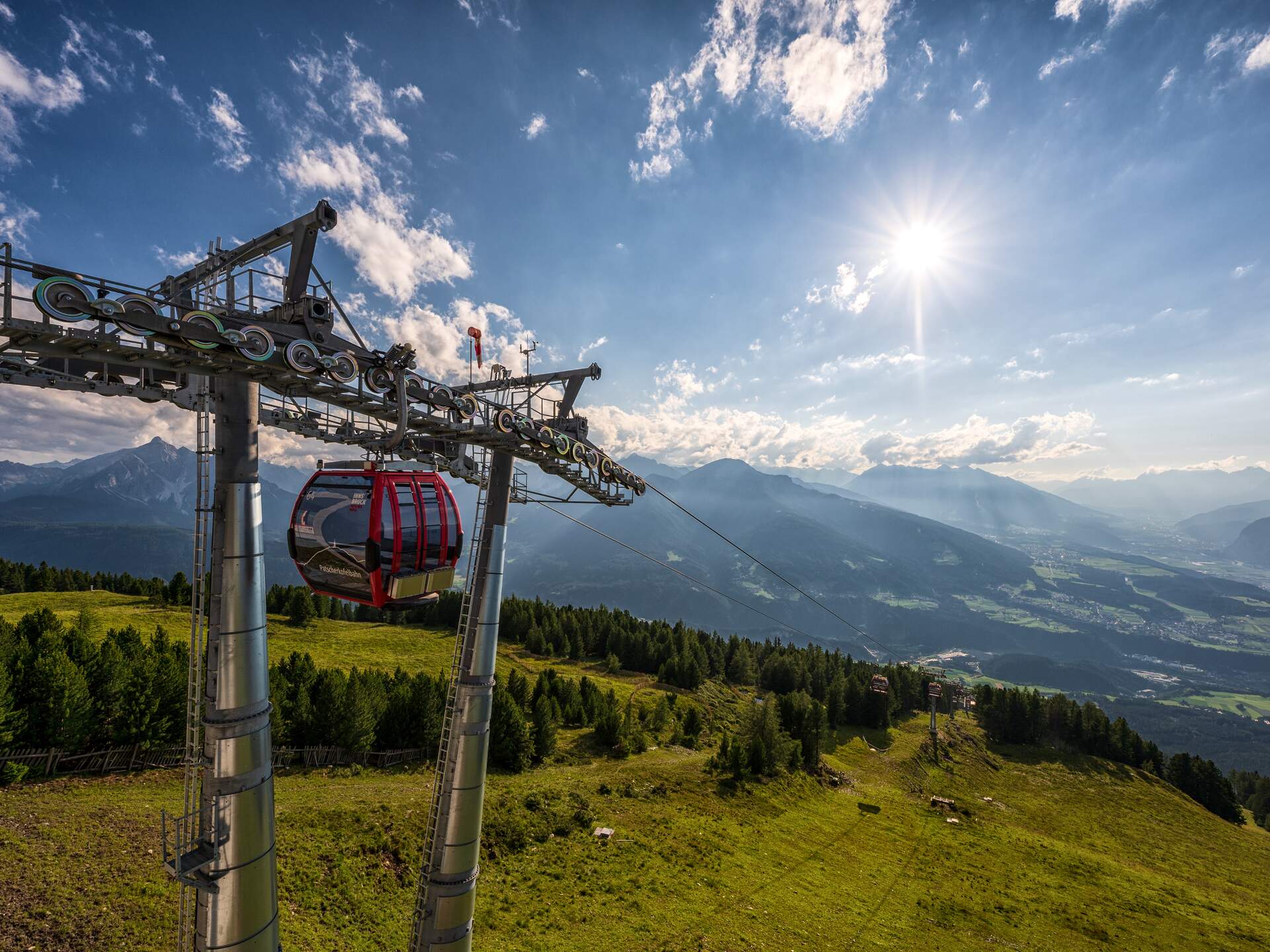 Rote Gondel der Patscherkofelbahn an Stahlseil vor Bergpanorama und blauem Himmel mit Sonne | © Innsbruck Tourismus, Markus Mair