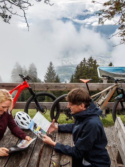 Zwei Personen mit Mountainbikes betrachten eine Karte vor Bergpanorama mit Wolken | © Erwin Haiden