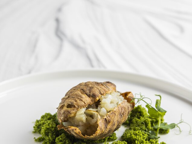 Jerusalem artichoke tartar with arugula crumbs on a white plate against a marble background