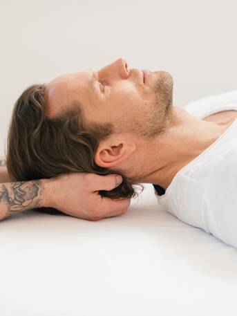 Mann erhält Nackenmassage, liegt entspannt auf weißer Liege