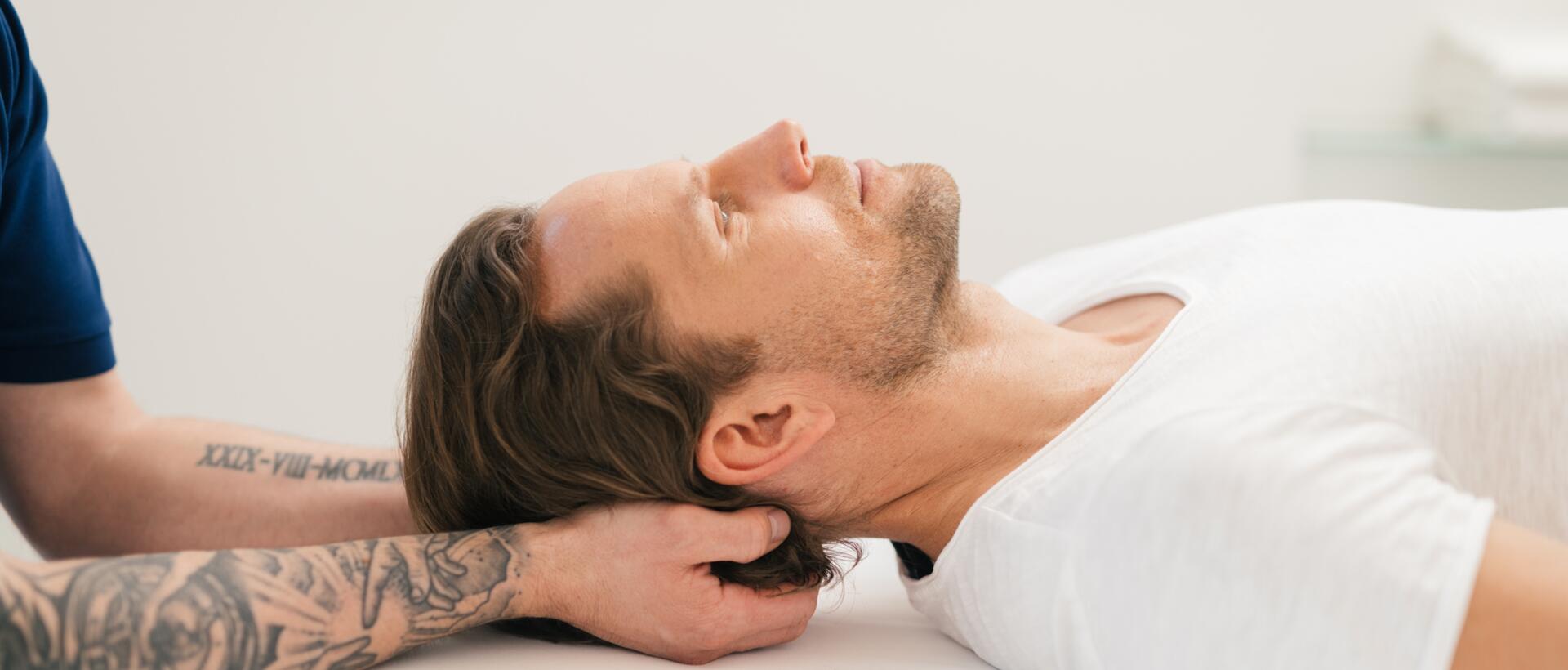 Mann erhält Nackenmassage, liegt entspannt auf weißer Liege