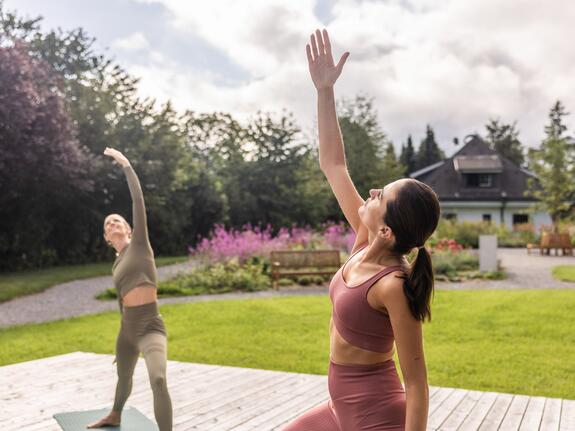 Zwei Frauen machen Yoga im Park, eine Hand erhoben