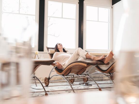 Frau entspannt auf Liege im Spa vor hellem Fenster